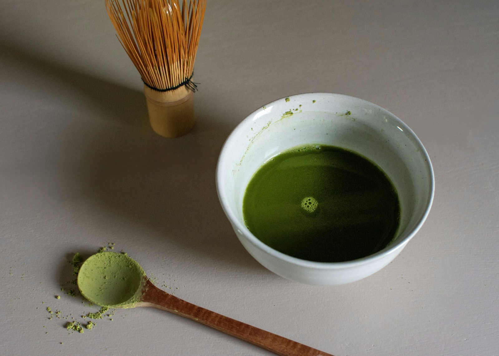白い茶碗に点てられた抹茶と茶筅、粉を掬った木のスプーン